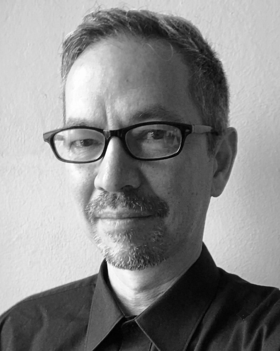 Julian Hockings — black-and-white portrait, glasses, dark shirt, calm direct gaze